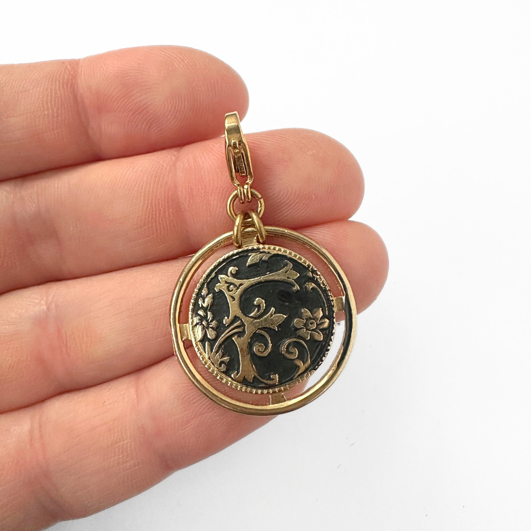 Large black and gold ornate letter "F" circular charm